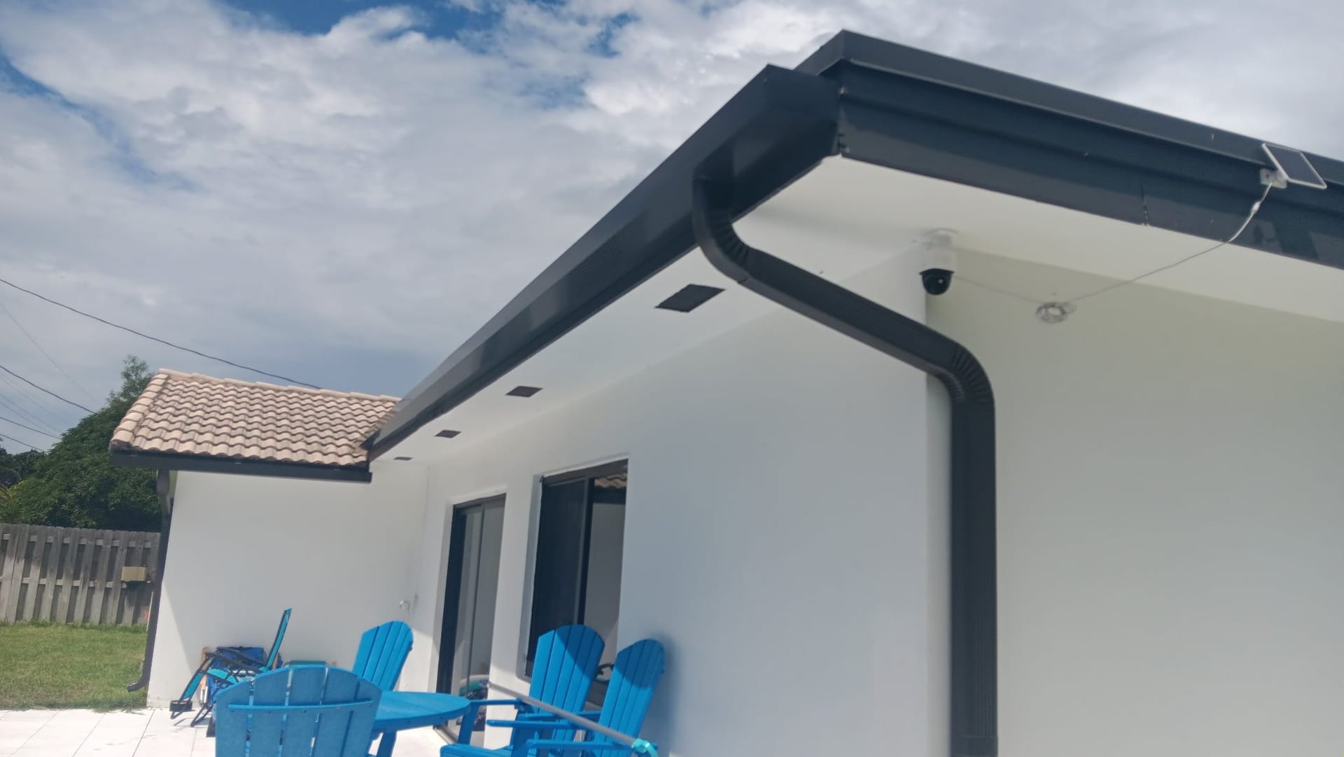 Dark bronze seamless gutter turning a roof corner with a downspout bending down a white wall